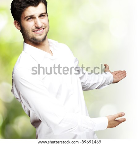portrait of a handsome young man gesturing welcome against a nature background