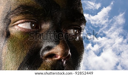 young soldier face with jungle camouflage against a blue sky background
