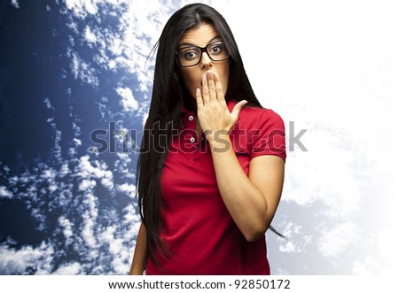 portrait of young woman covering her mouth with hand against a cloudy sky background