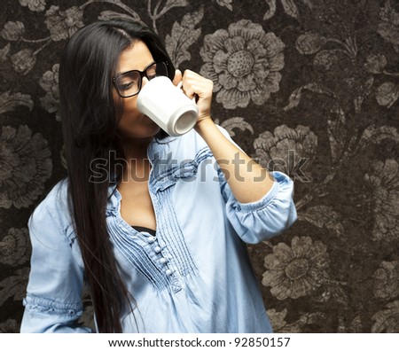 portrait of a pretty young woman drinking coffee on a cup against a vintage wall