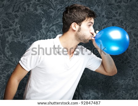 portrait of young man blowing a balloon against a vintage wall