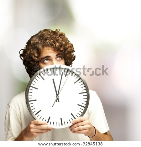 scared young man hidden behind a clock against a abstract background