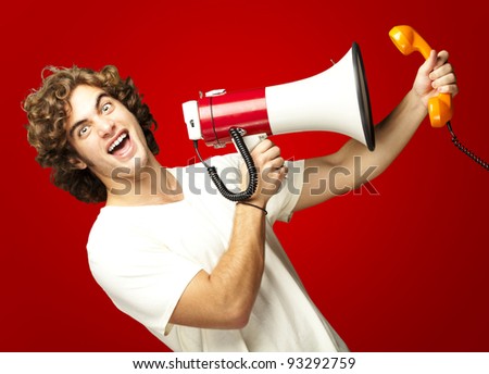 portrait of a young man shouting with a megaphone and talking on a vintage telephone over a red background