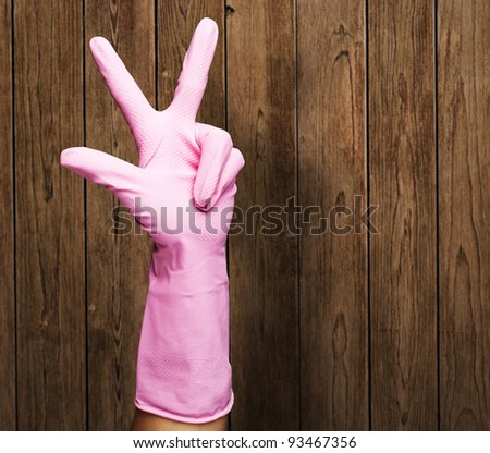 pink gloves of maid gesturing number three against a wooden wall