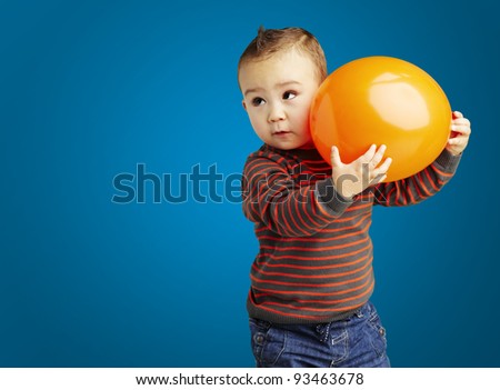 portrait of funny kid holding a big orange balloon over blue background