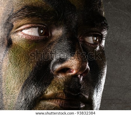 portrait of a young soldiers face painted with jungle camouflage against a grunge wall