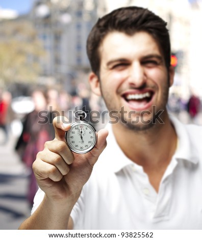 Portrait of a young man laughing and showing a stopwatch at a crowded place