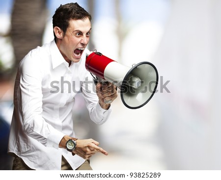 portrait of a young man screaming with a megaphone against a street background