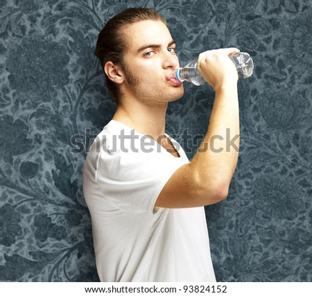 portrait of a young man drinking water against a vintage wall