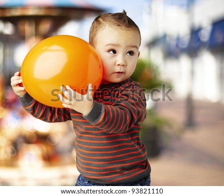 portrait of a funny kid holding a big orange balloon against a carousel
