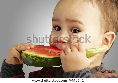 portrait of a handsome kid biting a watermelon over grey background