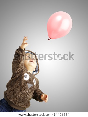 portrait of funny kid trying to hold a pink balloon over grey background