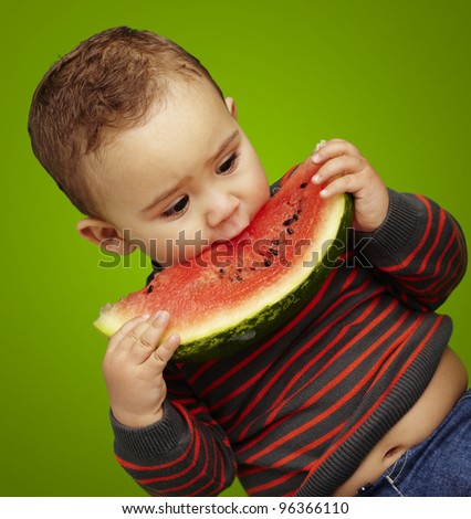 portrait of a handsome kid biting a watermelon over green background