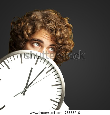 scared young man hidden behind a clock against a black background