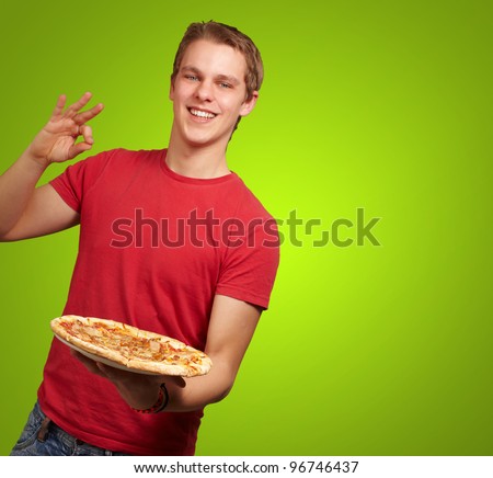 portrait of young man holding pizza and doing good gesture over green background