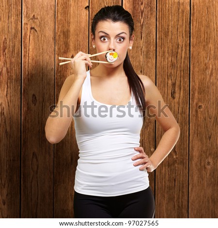 young woman covering her mouth with a sushi piece against a wooden background