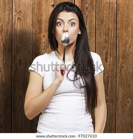 woman covering her mouth with a spoon against a wooden background