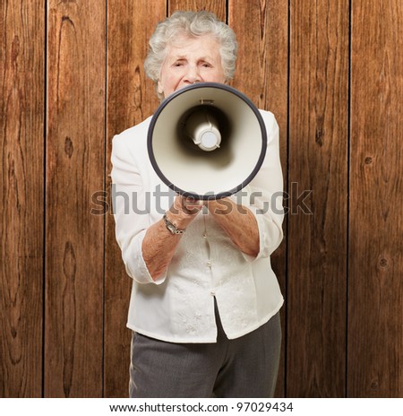 portrait of senior woman screaming with megaphone against a wooden wall