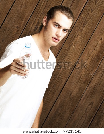 portrait of a handsome young man offering a water bottle against a vintage wall