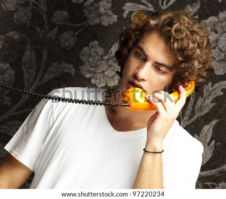 portrait of a young man talking on a vintage telephone against a vintage wall