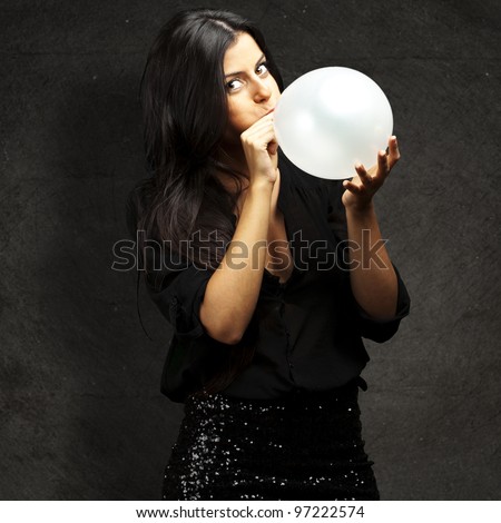portrait of a young woman blowing up a balloon against a grunge wall