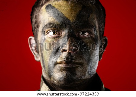 portrait of a young soldier face with jungle camouflage paint against a red background