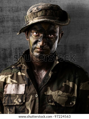 portrait of a young soldier face painted with jungle camouflage against a grunge wall