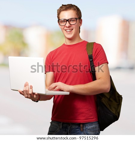 portrait of young man holding laptop and wearing backpack at city