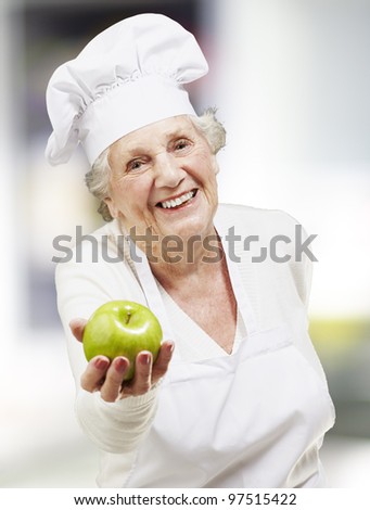 senior woman cook offering a green apple, indoor