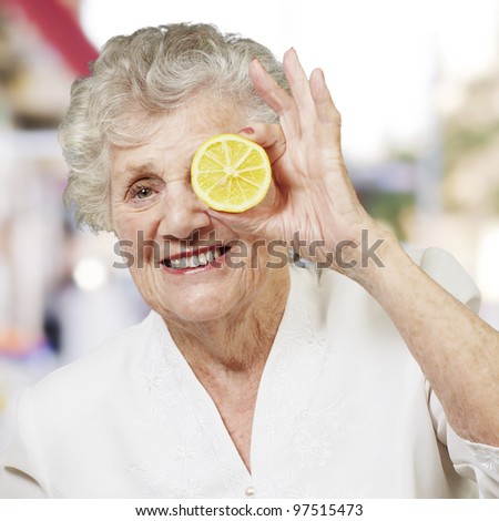 portrait of senior woman with lemon in front of her eye against a street
