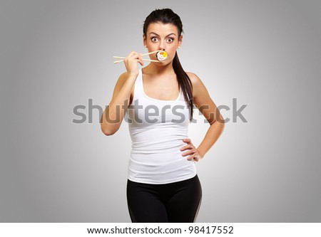 young woman covering her mouth with a sushi piece against a grey background
