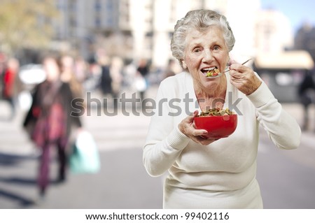 senior woman eating cereals out of a red bowl against a street background