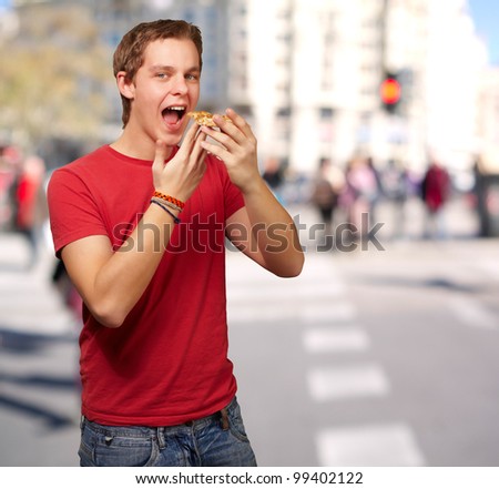 portrait of young man eating pizza at crowded street