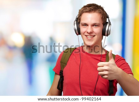 portrait of cheerful young student listening music and gesturing good with headphones indoor