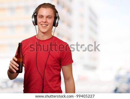 portrait of young man listening music and holding beer against a building