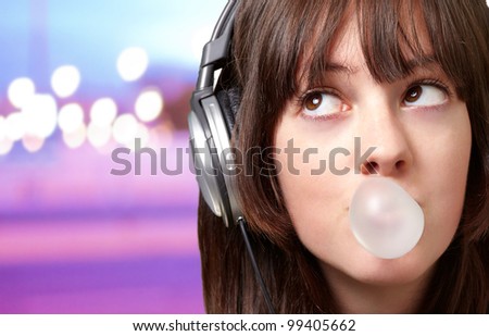 portrait of young woman listening to music with bubble gum over abstract lights