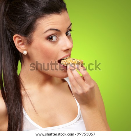 young healthy girl eating a cereal bar over a green background