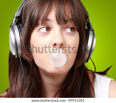 portrait of a young woman listening to music with a bubble gum over a green background