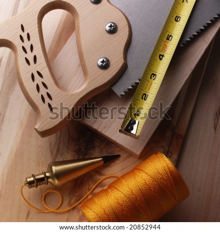 Wood working tools on a wooden background, including saw, ruler and plumb bob