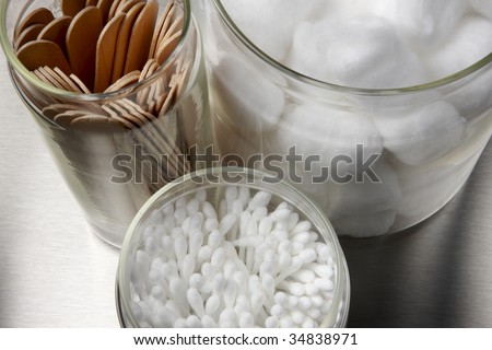 tongue depressors, cotton swaps and cotton balls in glass containers on a stainless surface