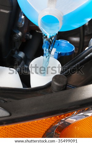 A gallon of blue windshield washer fluid being poured into tank under hood