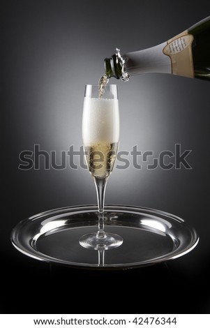 Champagne pours into flute which sit on a silver tray