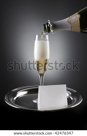 Champagne pours into flute sitting on silver tray with white place card including space for type