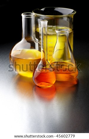 Flasks and beakers filled with bio fuels, shot on textured metal lab table with space for copy