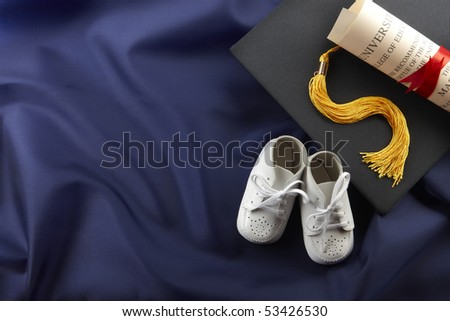 White baby shoes, cap, tassel and diploma shot on blue graduation gown with space for copy