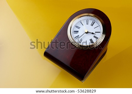wood and brass executive desk clock shot on yellow-orange background with space for copy