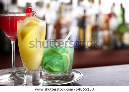 Three tropical mixed drinks sitting on silver tray, shot in bar with space for copy