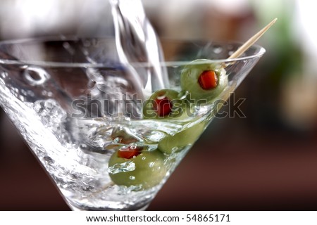 Macro shot of vodka pouring into a martini glass with green olives
