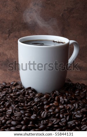 Steaming hot cup of coffee sitting in a pile of coffee beans with space for copy