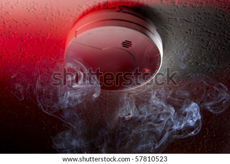 Close up shot of ceiling mounted smoke detector with white smoke and red warning light
